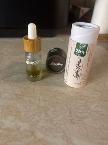 Ein Kunde zeigt das Fläschchen des 20% CBD-Öls neben der runden Verpackung auf einer Theke.