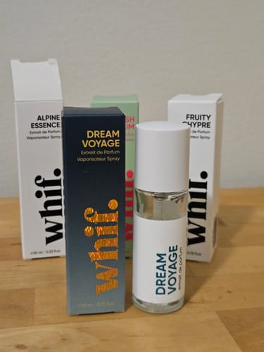 Customer's Dream Voyage perfume bottle and its dark box, shown with other fragrances from the brand on a wooden table.