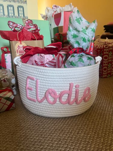 Customer's personalized white knitted basket with 'Elodie' in pink, filled with wrapped Christmas presents.