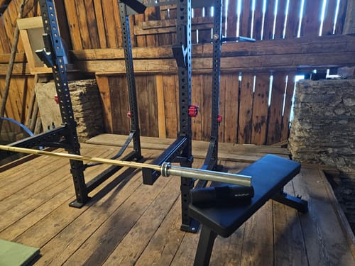 Kundenrezension der schwarzen R8 Klimmzugstange, die an einem Power-Rack in einem rustikalen Home-Gym montiert ist.