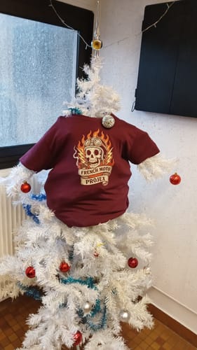 Le client montre son T-shirt bordeaux de la collection EREDITA, joliment exposé sur un sapin de Noël blanc.