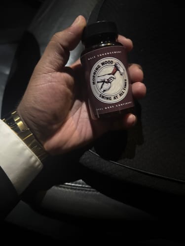 Customer's hand holding a small bottle of Morning Wood Capsules in a dimly lit car.
