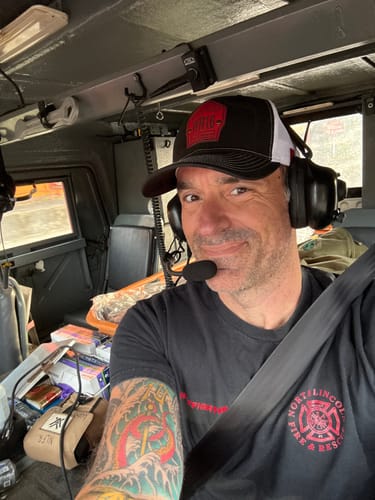 Reviewer smiling in a vehicle while wearing the black and white Shield Hat with a headset.
