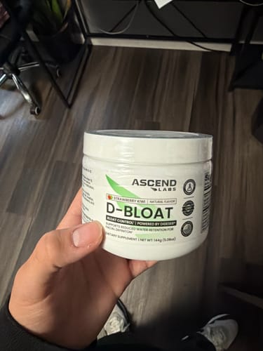 Customer holding a new, sealed white tub of D-BLOAT powder in their hand.