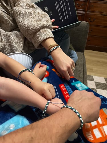 Close-up of a family's wrists, all wearing the woven DAVID Bracelet.