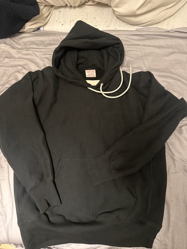 Customer's black Military Academy Reverse Weave Hoodie laid out flat on a bed.