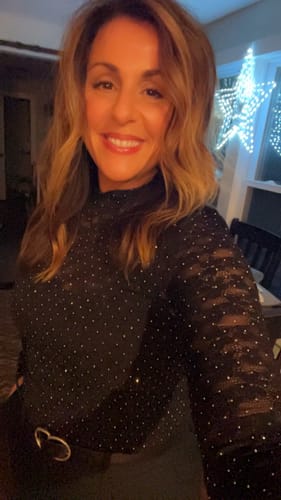 Reviewer smiling in the black, sparkly Twinkle In The Sky Lace Top indoors.