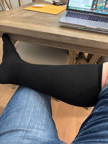 Customer sitting with their leg propped up, wearing the black Performance Eucalyptus Compression Socks.