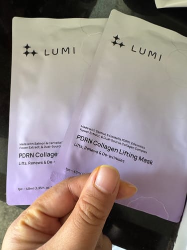 Reviewer's hand holding two PDRN Collagen Lifting Mask packages while making a finger heart gesture.