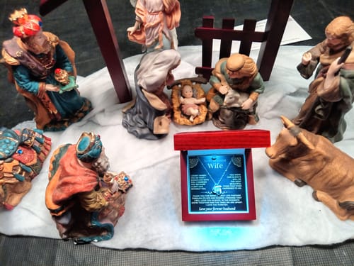 Customer's Love Knot Gift Set in its open, illuminated box, placed among nativity scene figurines.