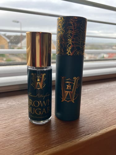 Customer's Brown Sugar travel perfume bottle and its dark, gold-accented case sitting on a wooden windowsill.