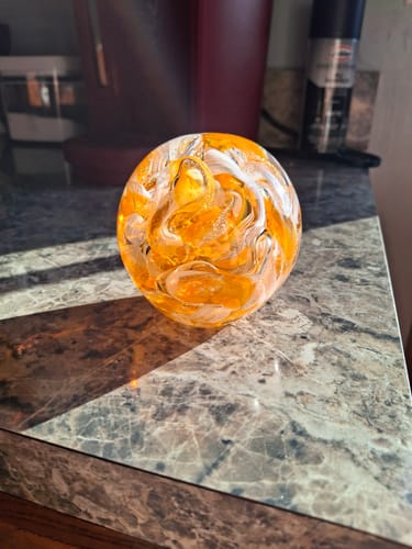 Customer's orange and white Cotton Candy Orb with Ash sitting on a marble countertop in the sun.