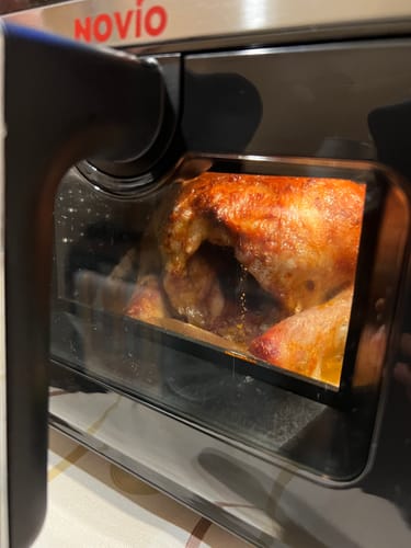 Client gătind un pui întreg, cu piele aurie, în friteuza Air Fryer Novio StonePro.