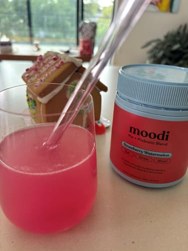 Reviewer's stemless wine glass filled with the pink Strawberry Watermelon drink, with the product tub sitting next to it.