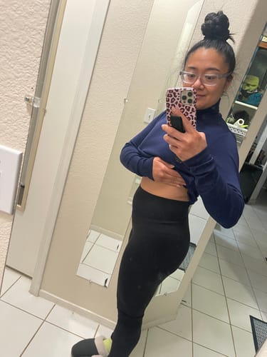 Reviewer lifts their top to show the high-waisted fit of the black Ellis Seamless Petite Tights.