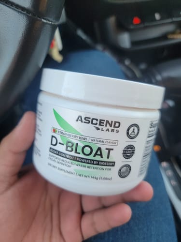 Customer holding a white tub of D-BLOAT strawberry kiwi powder inside a car.