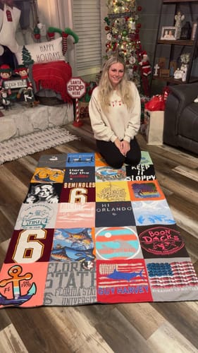 Customer kneeling behind her Premium T Shirt Quilt, spread out on the floor in front of a Christmas tree.