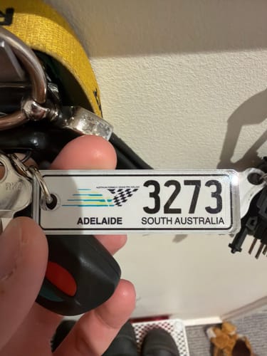 Customer holding a custom Grand Prix SA licence plate keychain with the number 3273 and the word 'Adelaide'.