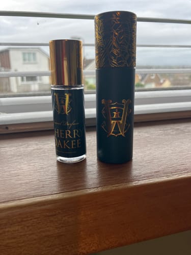 Customer's small bottle of Cherry Oakee perfume next to its dark travel case on a windowsill.