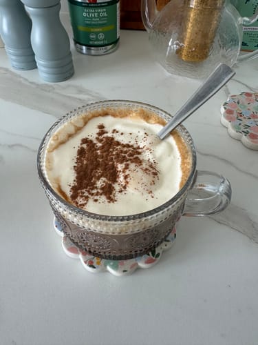 Reviewer's Choc Hazelnut Flavour drink served in a clear mug with a creamy topping and a sprinkle of cocoa.