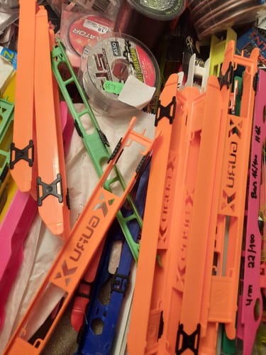 Recensent toont een verzameling feloranje Guru Rig Winders tussen ander visgerei.