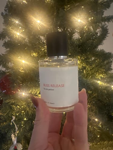 Customer holding a bottle of Bliss Release perfume in front of a lit, festive tree.