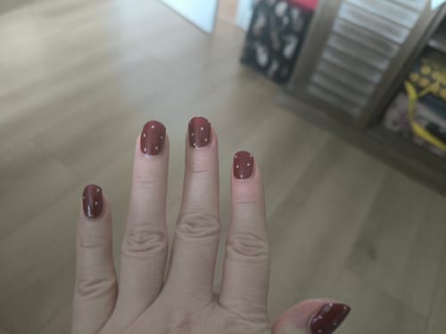 Kundenhand mit den 'Dainty Little Love' UV-Gelfolien in einem merlotroten Ton mit kleinen weißen Punkten.