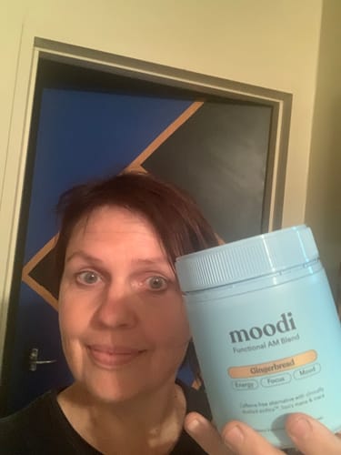 Reviewer smiling and holding a light blue tub of moodi Gingerbread blend.