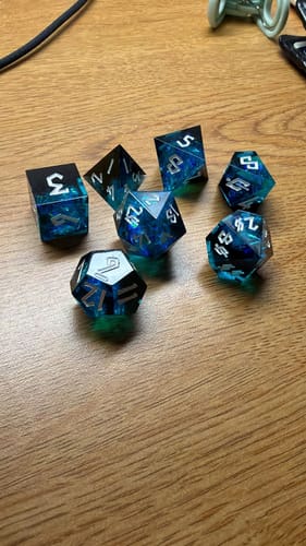 Reviewer's blue and black Moonbeam sharp-edged resin dice set on a wooden table.