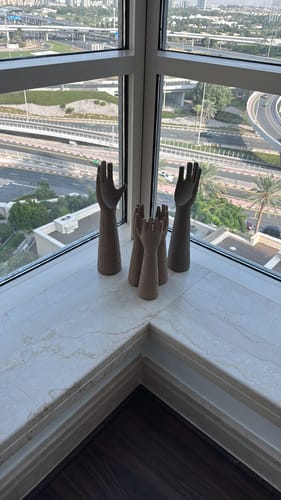 Reviewer's Raise Hand sculptures arranged as a family on a windowsill with a city view.