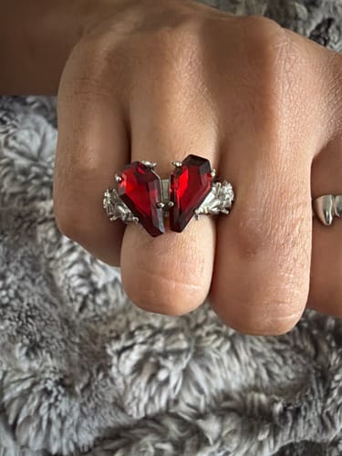 A reviewer's hand wearing the PROMISE RING, showing the detailed silver band and red coffin-shaped heart stone.