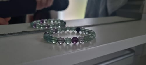Photo d'un client du bracelet fluorine aux perles facettées vertes et violettes, posé sur une étagère blanche.