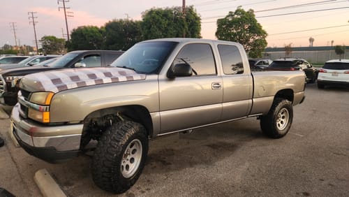 Customer's lifted silver pickup truck parked, showing the installed Upper Control Arms in the front wheel well.