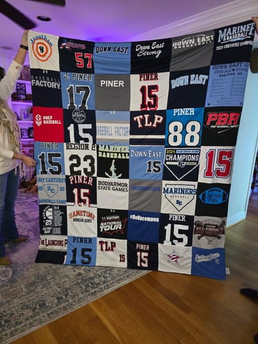Reviewer holding up a large Premium T Shirt Quilt made from their son's old sports jerseys.