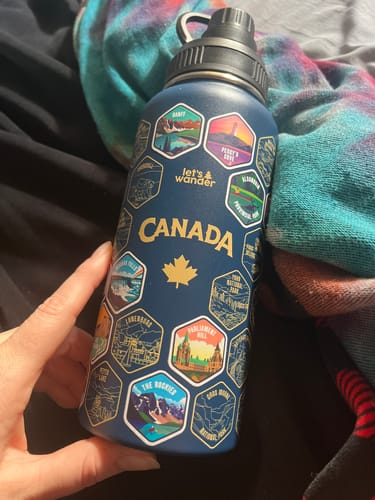 A reviewer holds up their blue Canada Bottle, which has several colorful stickers of landmarks applied to the front.