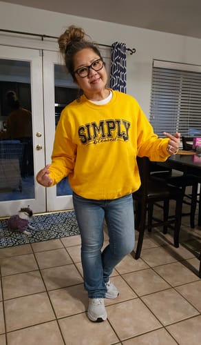 Reviewer smiling while wearing her oversized, yellow Simply Blessed Sweatshirt indoors.