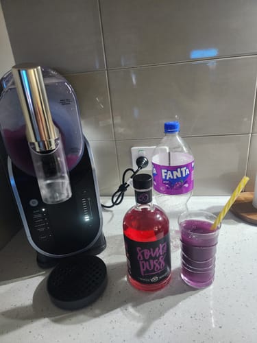 Reviewer's bottle of Sour Puss Watermelon on a counter with a slushie maker and a prepared purple slushie.