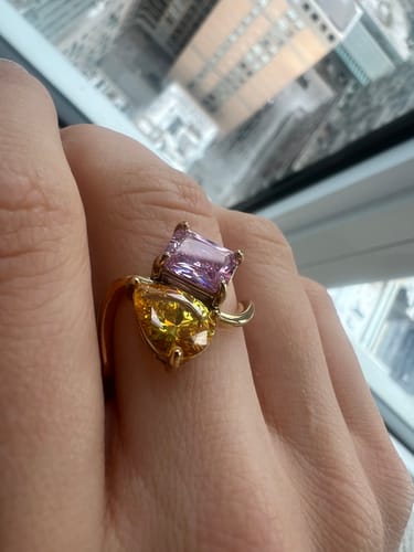 Close-up of a reviewer's hand wearing the Navae Birthstone Ring with a yellow pear-cut and pink radiant-cut stone.