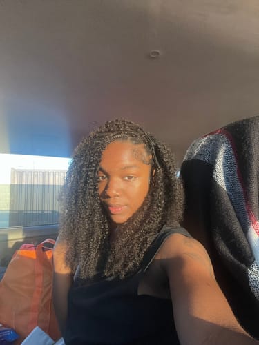 Reviewer in a car showing their full, kinky curly hair extensions in natural sunlight.