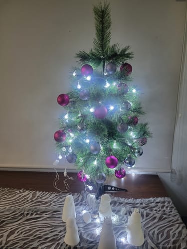 Un cliente muestra las esferas navideñas de color lila decorando un pequeño árbol de Navidad con luces.