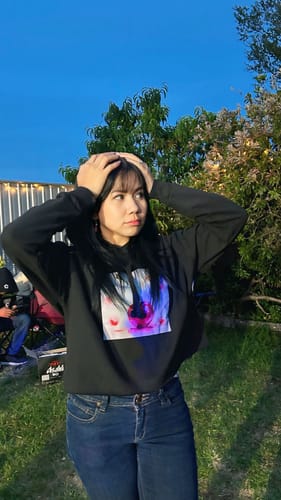 Reviewer outdoors wearing the black ladies cropped hoodie with a colorful graphic print and blue jeans.