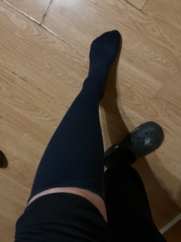 Kunde der viser pasformen af en sort Støttestrømpe på benet.