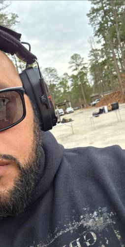 Partial view of a reviewer wearing a headset with the black MX Plate at an outdoor range.