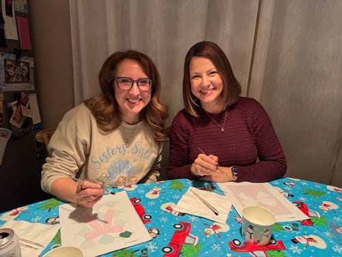 Two customers smiling while using the Merry Christmas Mini Paintings set at a festive table.