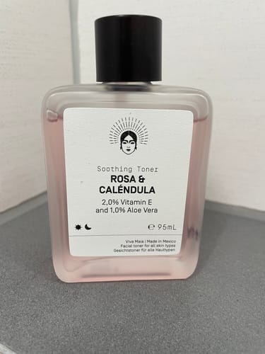 A reviewer's bottle of Soothing Toner - Rosa & Caléndula, a pink liquid in a clear square bottle with a black cap.