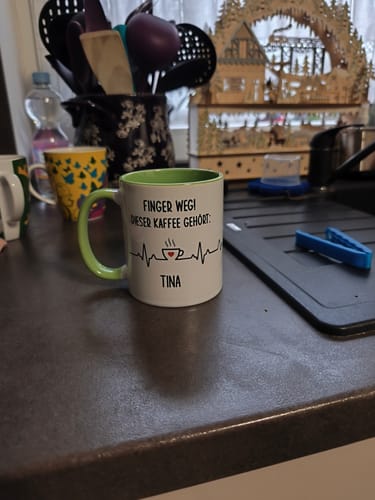 Ein Kunde zeigt die personalisierte „Finger Weg!“-Tasse mit dem Namen „Tina“ auf einer Küchentheke.