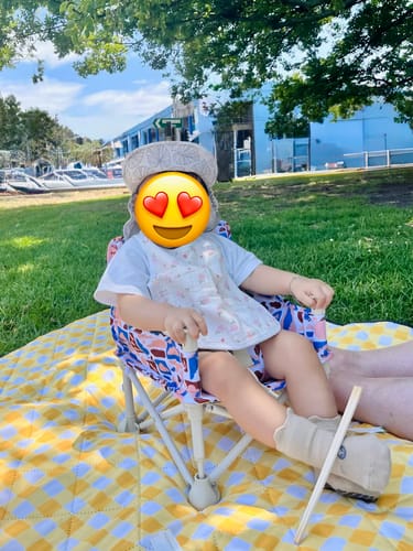 Customer's baby sitting in the colourful Amy baby chair v2 on a picnic blanket outdoors.