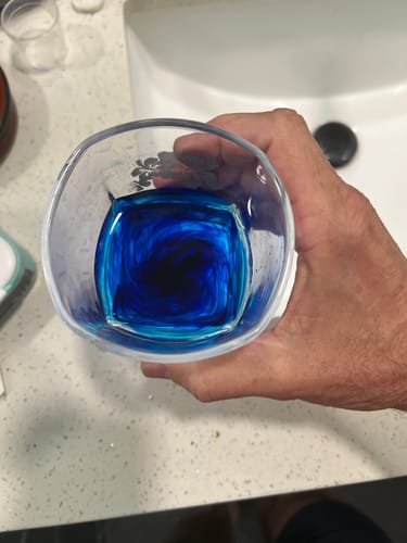 A reviewer holds a glass showing the vibrant blue Meraki Blu Methylene Blue dye swirling in liquid.