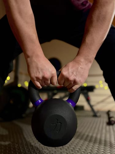 Customer holding a black cast iron kettlebell with two hands, showing the purple handle markings.