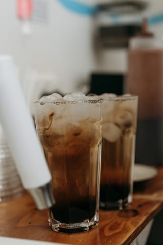 Reviewer's photo of two tall glasses of Lemon Myrtle Iced Tea filled with ice on a wooden shop counter.